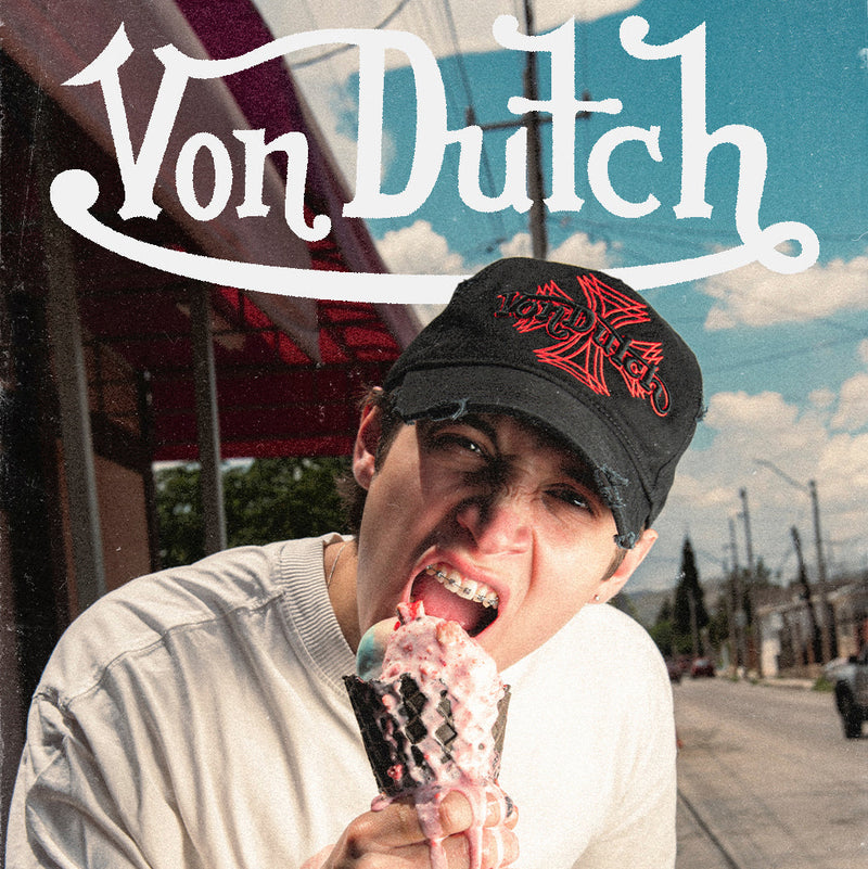 A person outdoors wearing a black baseball cap with a red graphic, a white T-shirt, and dark jeans, holding an ice cream cone. Large white text at the top reads 'Von Dutch', with 'NEW DROP' and a '2CAP' logo near the bottom.